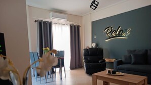 Ein modernes Wohnzimmer mit einer Couch, einem Couchtisch, einem schwarzen Sessel, einem Essbereich mit Tisch und Stühlen und einer Wand mit dem Schriftzug 'Relax'.