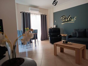 A modern living room with a sofa, a coffee table, a black armchair, a dining area with a table and chairs, and a wall with a 'Relax' sign.
