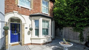 A residential property with a blue door, a bay window, and a small garden with a planter. - Peaceful 4-Bed Home in Aylesbury (Aylesbury)