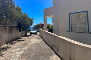 Een smalle straat met een betonnen muur aan de ene kant en een gebouw met een blauw omlijst raam aan de andere kant.