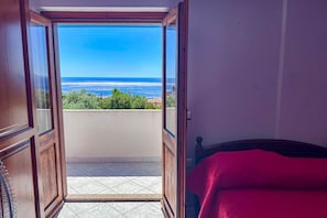 A room with a wooden door leading to a balcony with a view of the ocean. - Appartamento Tuttavista (Cala Gonone)