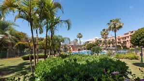 A pool area surrounded by palm trees and greenery, with a clear blue sky. - 'Inner Paradise' Apartment with Shared Pool, Wi-Fi and Air Conditioning (Atalaya Isdabe)