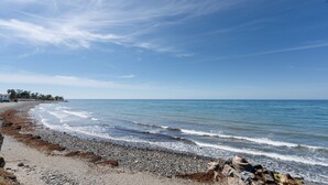 A beach with a rocky shoreline, a clear sky, and a distant shoreline with buildings. - 'Inner Paradise' Apartment with Shared Pool, Wi-Fi and Air Conditioning (Atalaya Isdabe)