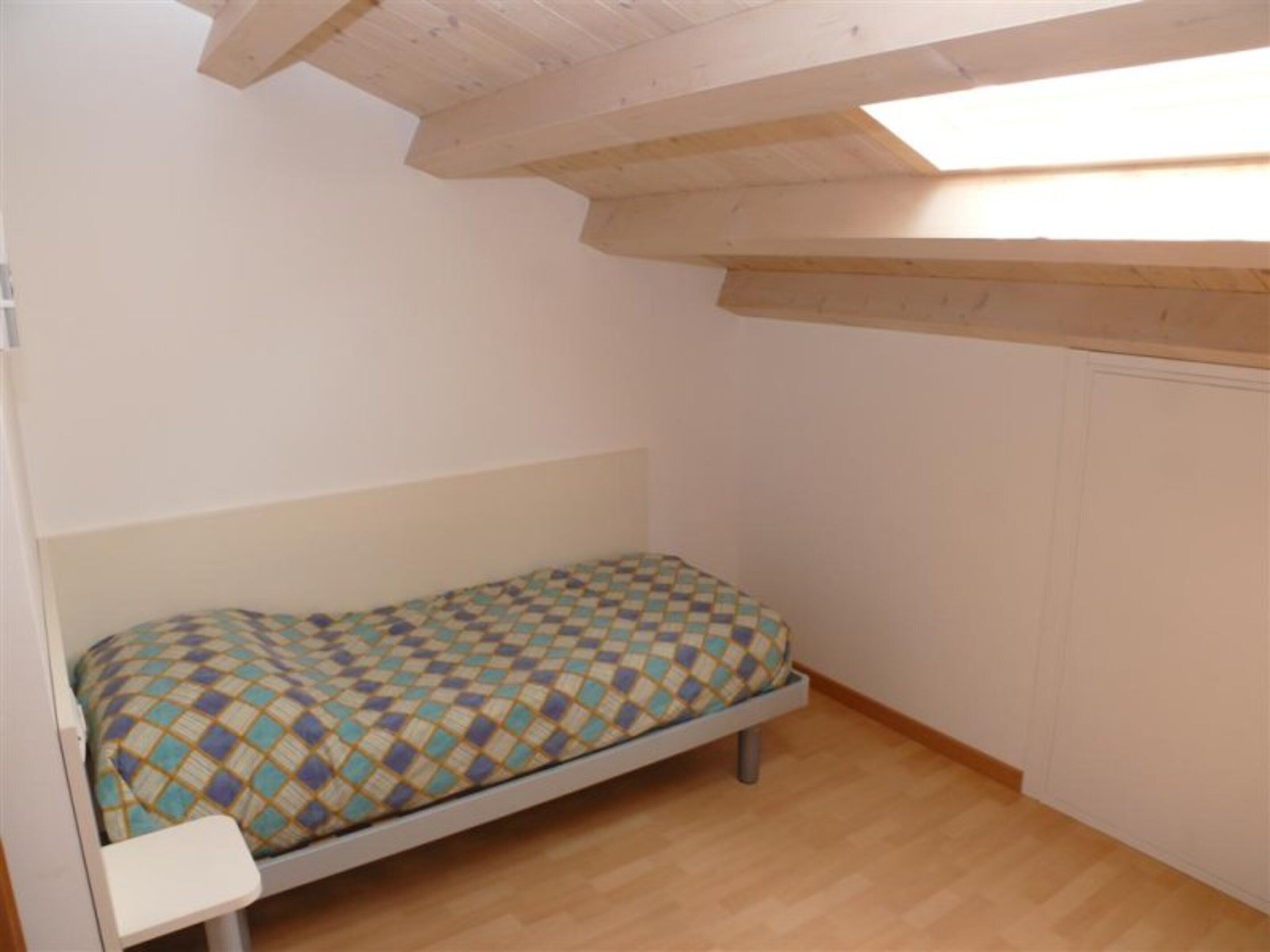 Un lit simple avec un matelas à motifs, dans une pièce au plancher en bois et au plafond en pente.
