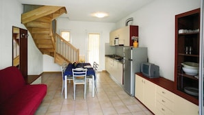 A compact kitchen with a built-in stove, a refrigerator, and a wooden staircase. - Shared Pool and Olive Orchard Garden Accommodation (San Michele al Tagliamento)