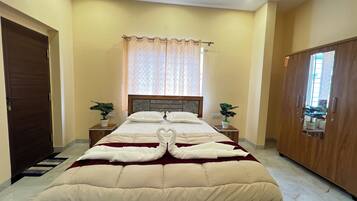 A hotel room with a bed, two bedside tables with plants, a wooden wardrobe, and a window with curtains.