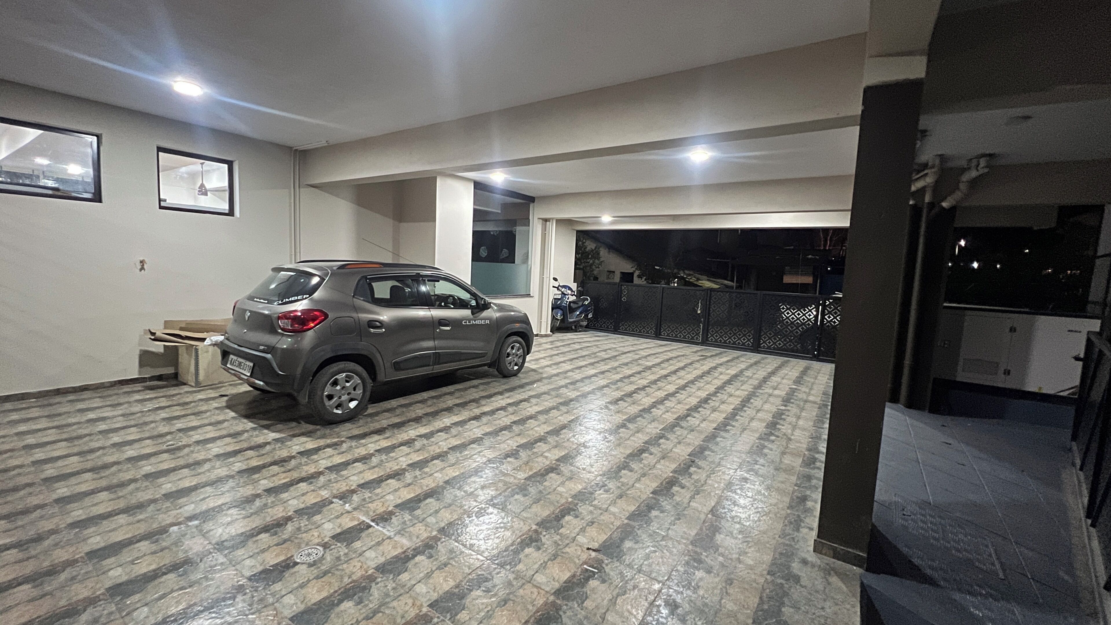 Um carro estacionado em uma garagem com piso de azulejos, uma motocicleta e um aparelho de iluminação fixado na parede.
