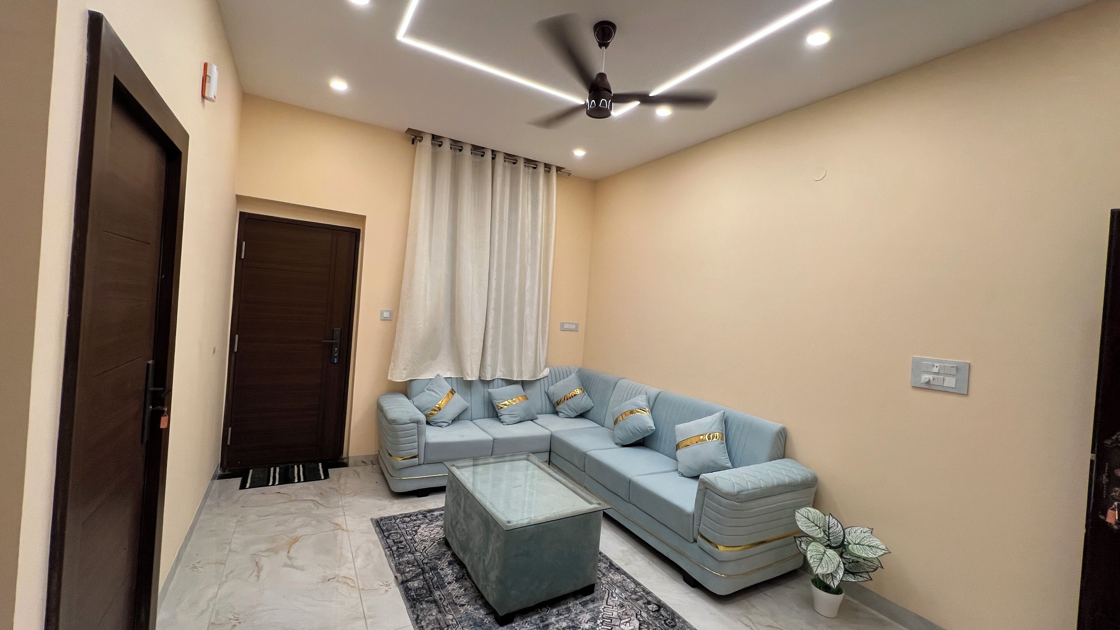 Una sala de estar moderna con un sofá modular, una mesa de centro de vidrio, un ventilador de techo y una planta en maceta.