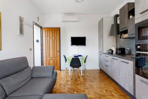 Uma cozinha moderna com televisão, mesa de jantar e sofá cinzento.