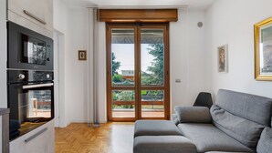 A modern living room with a grey sofa, a built-in oven, and a sliding glass door leading to an outdoor area. - Bed and Breakfast 'Villa Giusy' with Private Garden (Verdellino)