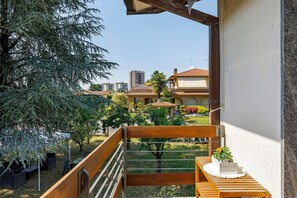 En balkon med en træbænk, et lille bord med en plante og udsigt over et boligområde med huse og træer.