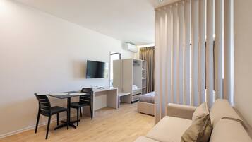 A modern living room with a sofa, a dining table with chairs, a TV mounted on the wall, and a wardrobe.