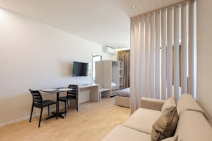 Ein modernes Wohnzimmer mit einer Couch, einem Esstisch mit Stühlen, einem an der Wand montierten Fernseher und einem Kleiderschrank.