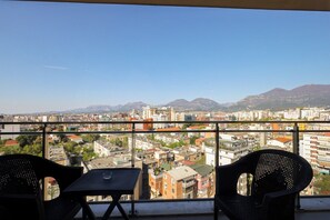 Ein Balkon mit zwei Stühlen und einem Tisch mit Blick auf eine Stadtlandschaft aus Gebäuden und Bergen.