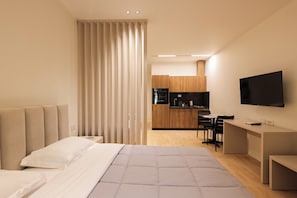 Ein modernes Hotelzimmer mit Bett, Schreibtisch, Fernseher und einer Küchenzeile.