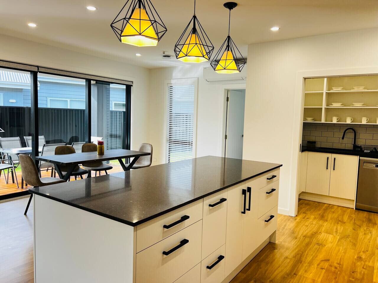Una cocina moderna con una isla central, luces colgantes y una zona de comedor con sillas.