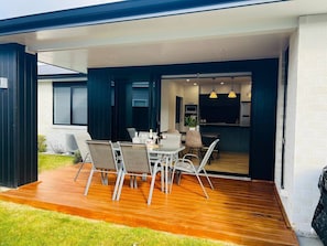 An outdoor patio with a dining table and chairs, a wooden deck, and a view into the house. - Entire Luxurious 4 Bedroom House (Taupō)