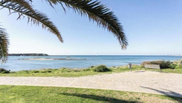 En kuststig som leder till en strand med fri utsikt över havet och det avlägsna landskapet.