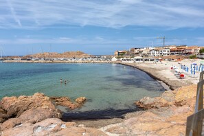 Eine Küstenlandschaft mit felsigem Gelände, klarem Wasser und einem Strand mit Sonnenschirmen.