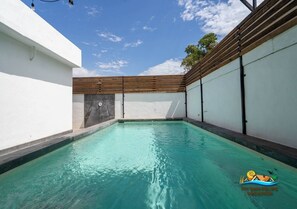 Une piscine avec une terrasse en bois et un mur blanc d’un côté.