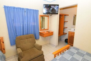 A small room with a brown chair, a bed with a blue and white checkered bedspread, a television mounted on the wall, a wooden shelf, and a mirror. - San Felipe Studio One (San Felipe)