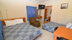 Ein Zimmer mit zwei Betten, einem Sessel, einem Fernseher und einem Schreibtisch.