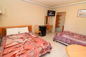 A hotel room with two beds, a desk, a chair, a television, and a small table.