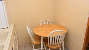 Un petit coin repas avec une table ronde en bois et deux chaises blanches.