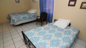 Une chambre avec deux lits, une chaise et une fenêtre avec des rideaux bleus.