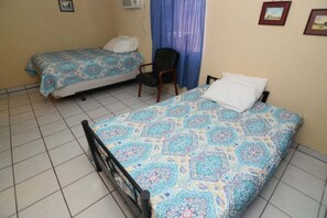A room with two beds, a chair, and a window with blue curtains. - San Felipe Studio Fout (San Felipe)