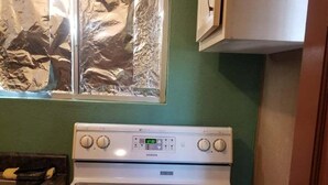 Une cuisine avec un fourneau, une fenêtre recouverte de papier d’aluminium et une porte.