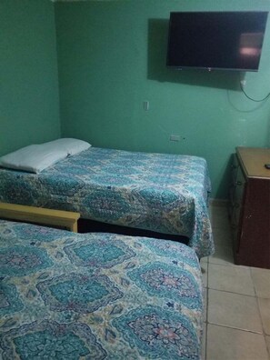 Ein Zimmer mit zwei Betten, einem an der Wand befestigten Fernseher und einem Holzschrank.