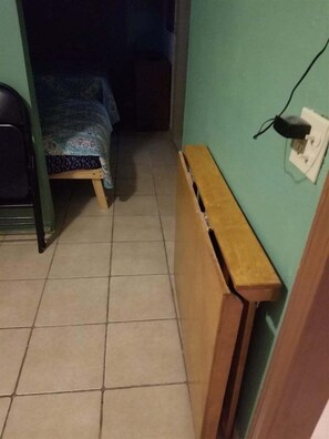 Ein schmaler Flur mit einer Holzbank, einem Bett mit gemusterten Betttextilien und einer Steckdose.