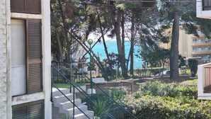 Ein Wohngebäude mit einer Treppe zu einem Balkon, umgeben von Bäumen und Blick aufs Meer.