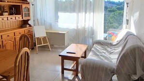 Ein Wohnzimmer mit einer Couch, einem Esstisch, Stühlen, einem kleinen Tisch und Blick durch große Fenster.