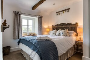 Un dormitorio con una cama grande, una ventana con cortinas, un cabecero de madera y una mesita de noche con lámpara.