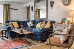 Un salon avec un canapé bleu, une table basse en bois, un fauteuil en cuir marron, un miroir et une horloge au mur.
