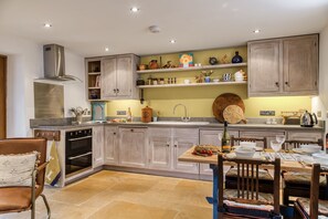 Una cocina con armarios de madera, horno empotrado, mesa de comedor con sillas y diversos utensilios y adornos de cocina.