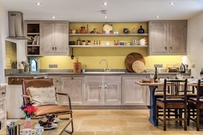 Une cuisine avec des meubles en bois, un coin repas avec des chaises, un îlot central, ainsi qu’une variété d’ustensiles de cuisine et d’objets de décoration disposés sur des étagères.