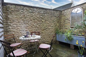 Un mur de pierre, une table ronde entourée de chaises et une fenêtre donnant sur le ciel.