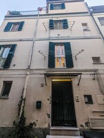 Un edificio a più piani con un ingresso centrale, diverse finestre con persiane e un balcone ben visibile.