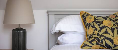 A bed with white bedding, a dark lamp on a wooden nightstand, and a floral pillow.