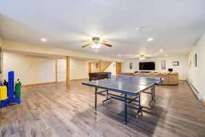 A spacious room with a ping pong table, a sofa, and a television.