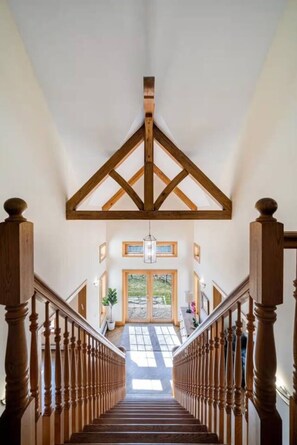 A grand staircase with wooden balusters leading to a landing with a large window and a view of the outdoors.