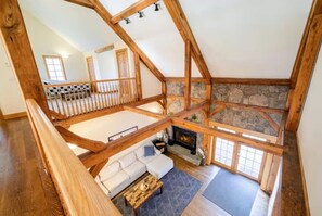 A spacious loft with a stone fireplace, wooden beams, and a view of the interior. - Luxe 6BR Group Retreat | Hot Tub, Fire Pit + Pond (Liberty)