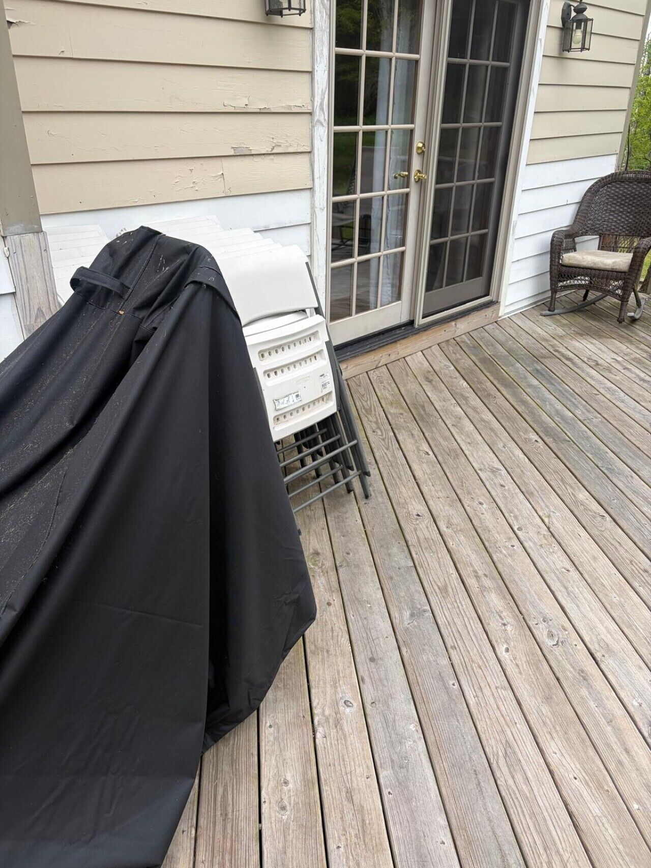 A covered grill on a wooden deck with a sliding glass door and a wicker chair.