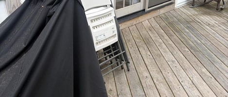 A covered grill on a wooden deck with a sliding glass door and a wicker chair.