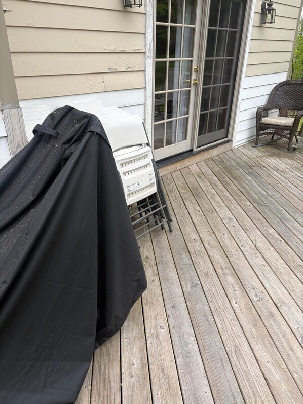 A covered grill on a wooden deck with a sliding glass door and a wicker chair.