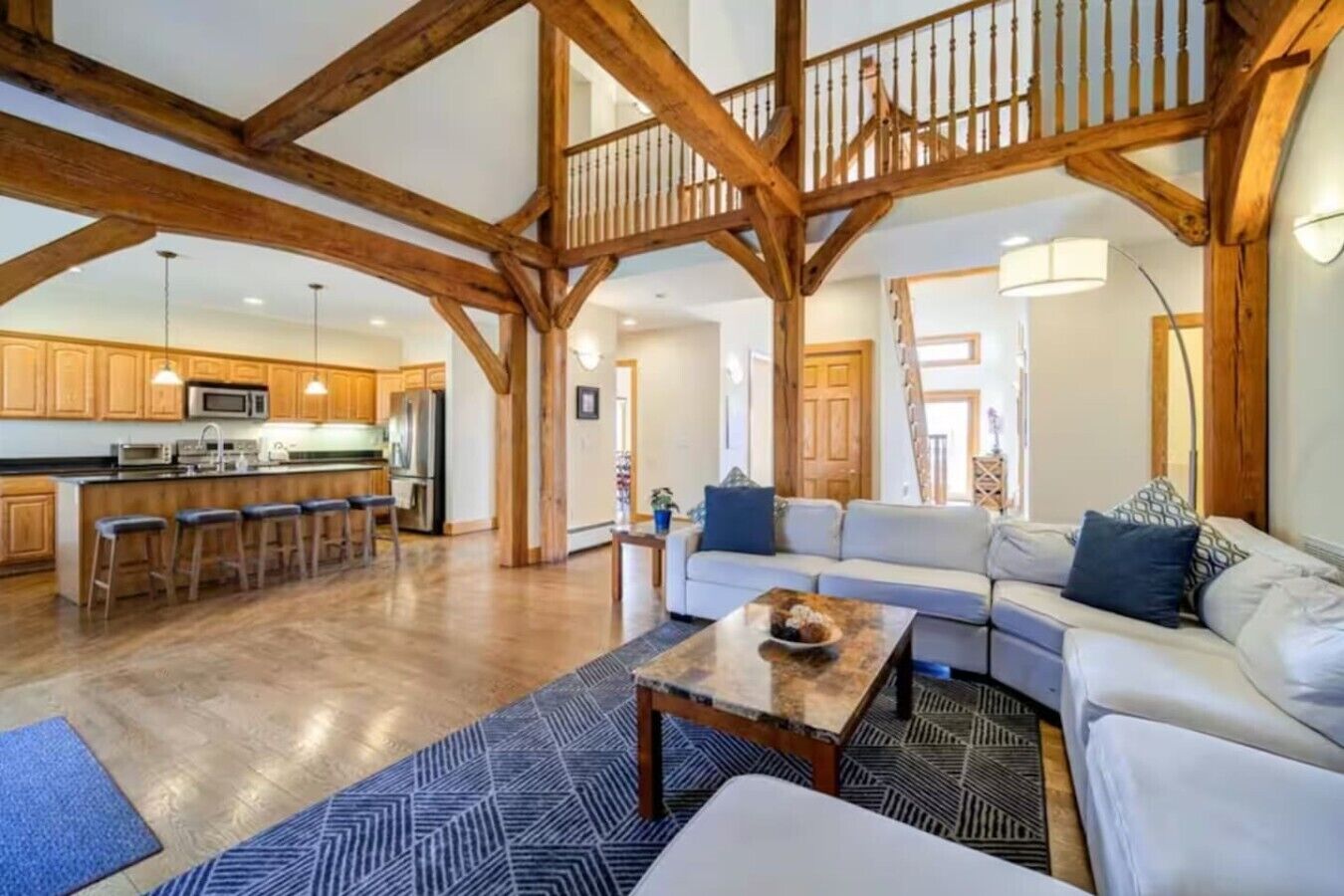 A spacious living area with a wooden ceiling, a kitchen with modern appliances, and a staircase leading to an upper level.