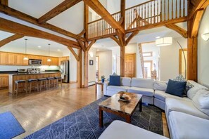 A spacious living area with a wooden ceiling, a kitchen with modern appliances, and a staircase leading to an upper level.